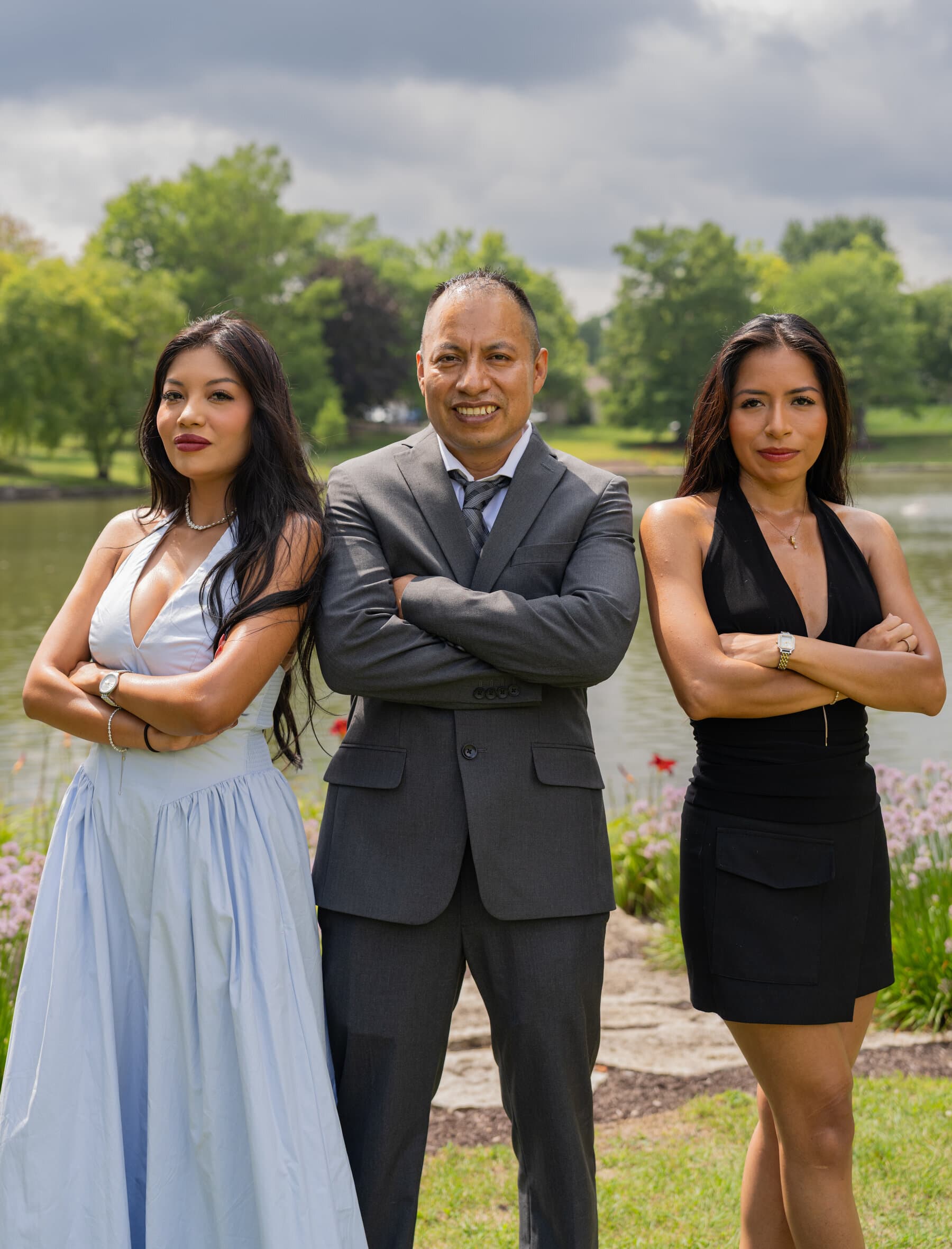 Father and two daughters posing arms crossed by a park lake